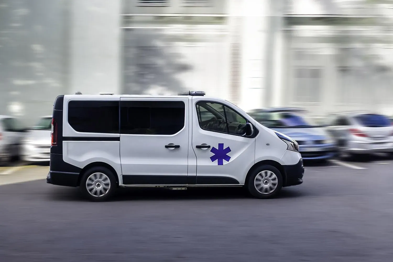 Véhicule sanitaire léger blanc roulant sur un parking