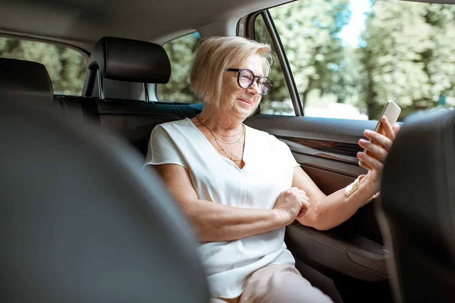 Passagère souriante à l'arrière d'un véhicule, téléphone en main